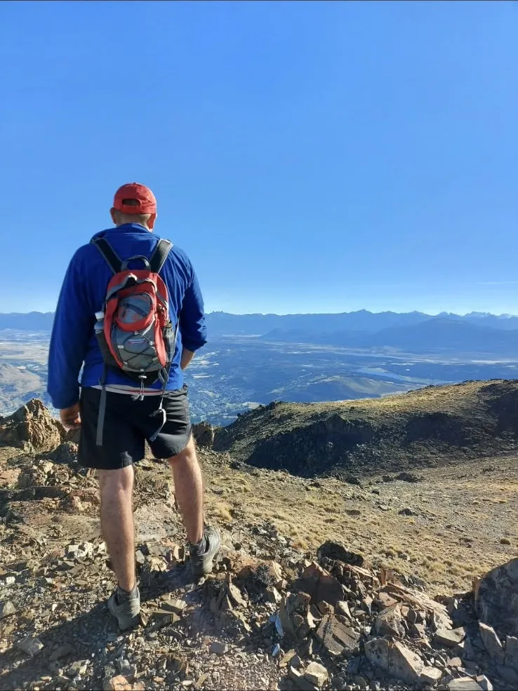 Persona con mochila mirando el valle desde la cumbre de un cerro