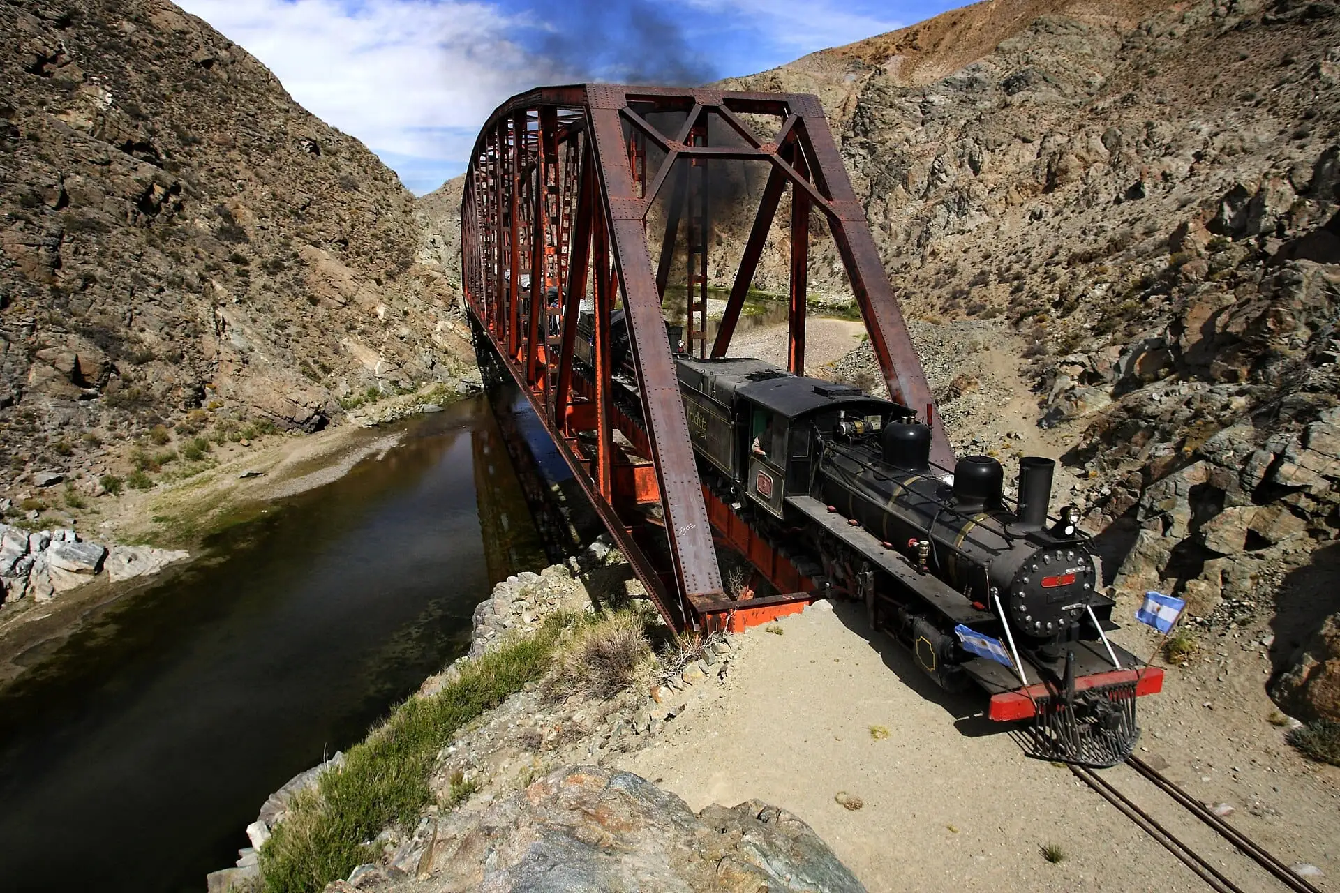 Locomotora a vapor de La Trochita cruzando un puente sobre un río (foto de ejemplo)